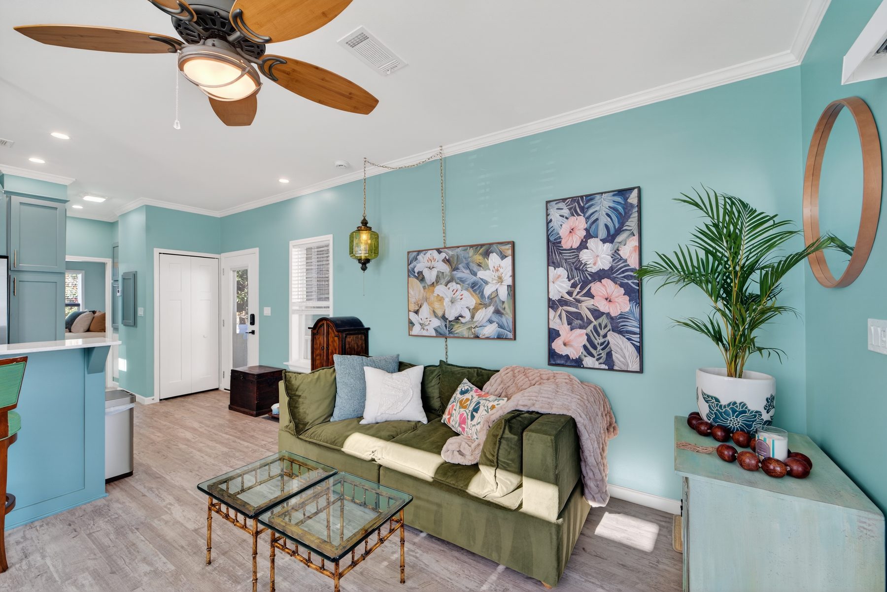 Living room with green velvet sofa, tropical art, and brass mirror
