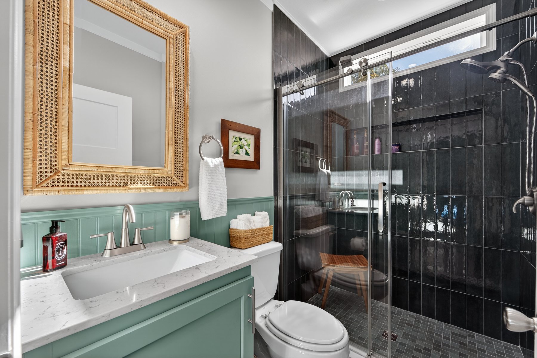 Renovated bathroom with fully tiled walk-in shower, quartz vanity, and cane mirror